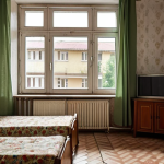 "A cozy, yet modest apartment interior in a Soviet-era building in Moldova. The furniture is simple, reflecting an affordable living space. Outside the window, a typical Moldovan residential street scene can be observed."
